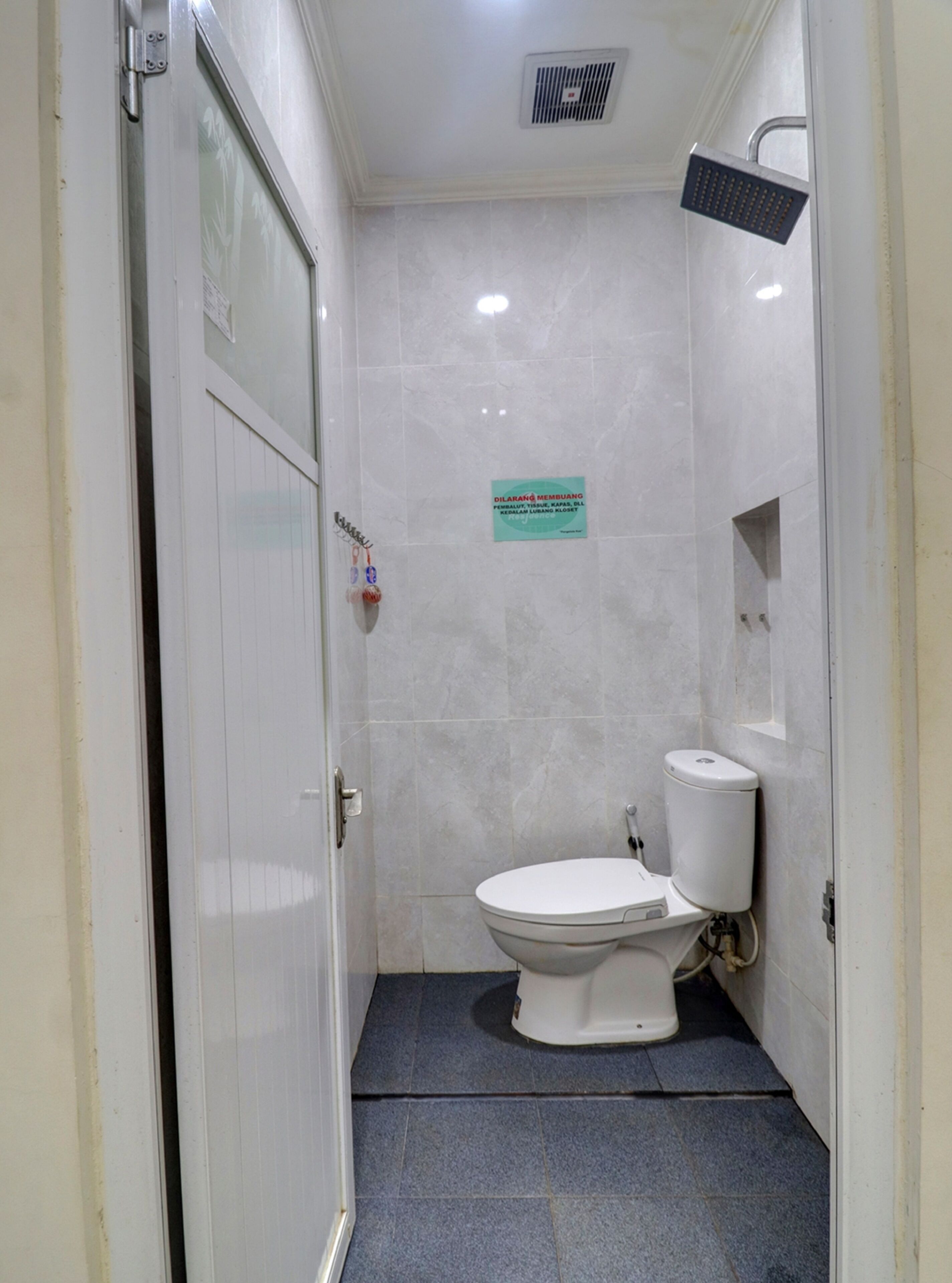 Une petite salle de bain compacte, avec des toilettes blanches, une pomme de douche et un panneau accroché au mur.