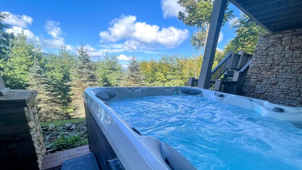 A hot tub with a stone wall and a view of trees and sky. - 4 Bedroom + 4 Bathroom Mountain Home at 4,700ft Views of Blue Ridge Mts + Big Bald + Spa + Elevator (Mars Hill)