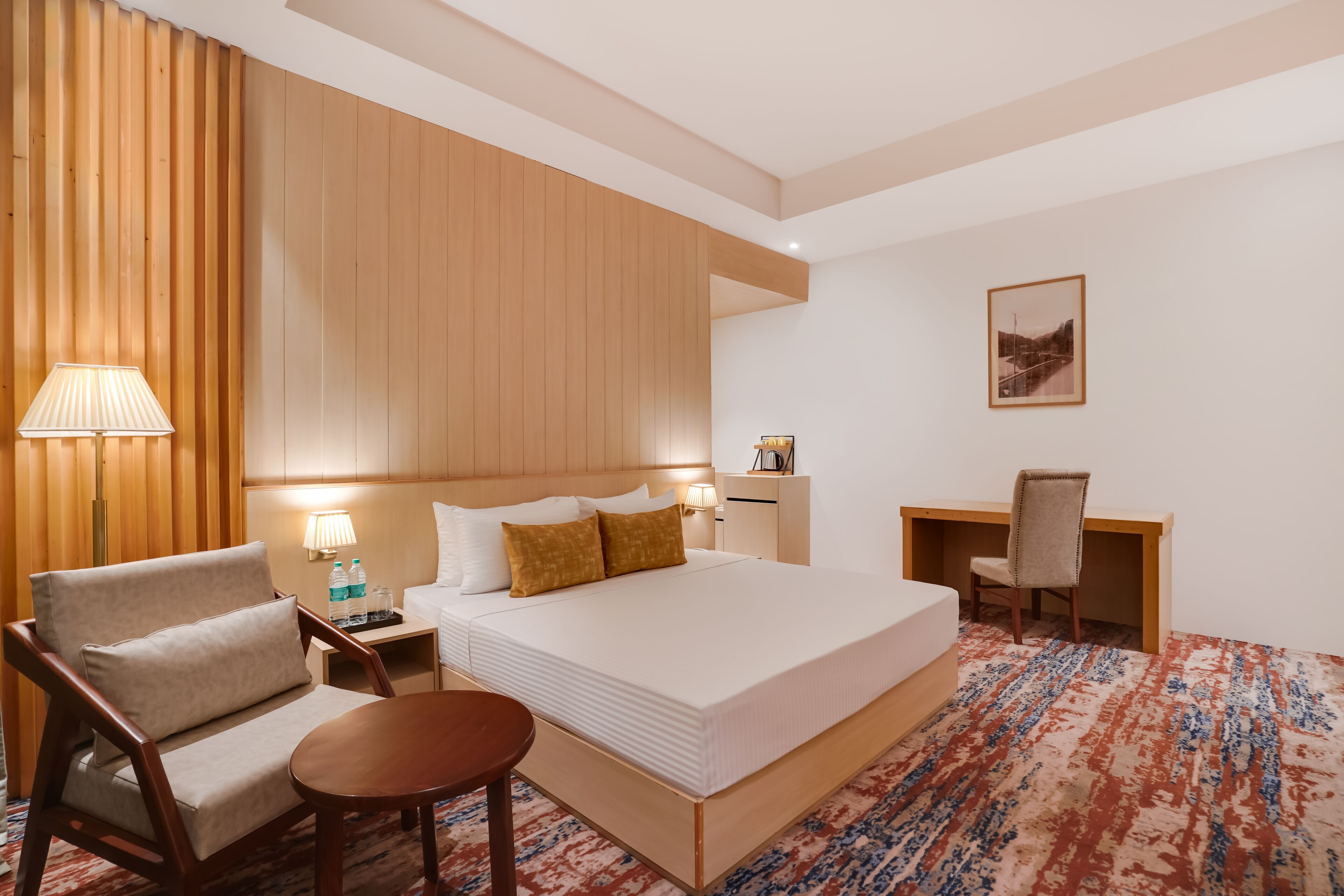 Una habitación de hotel con una cama grande, un escritorio, una silla, una mesita pequeña y una lámpara.