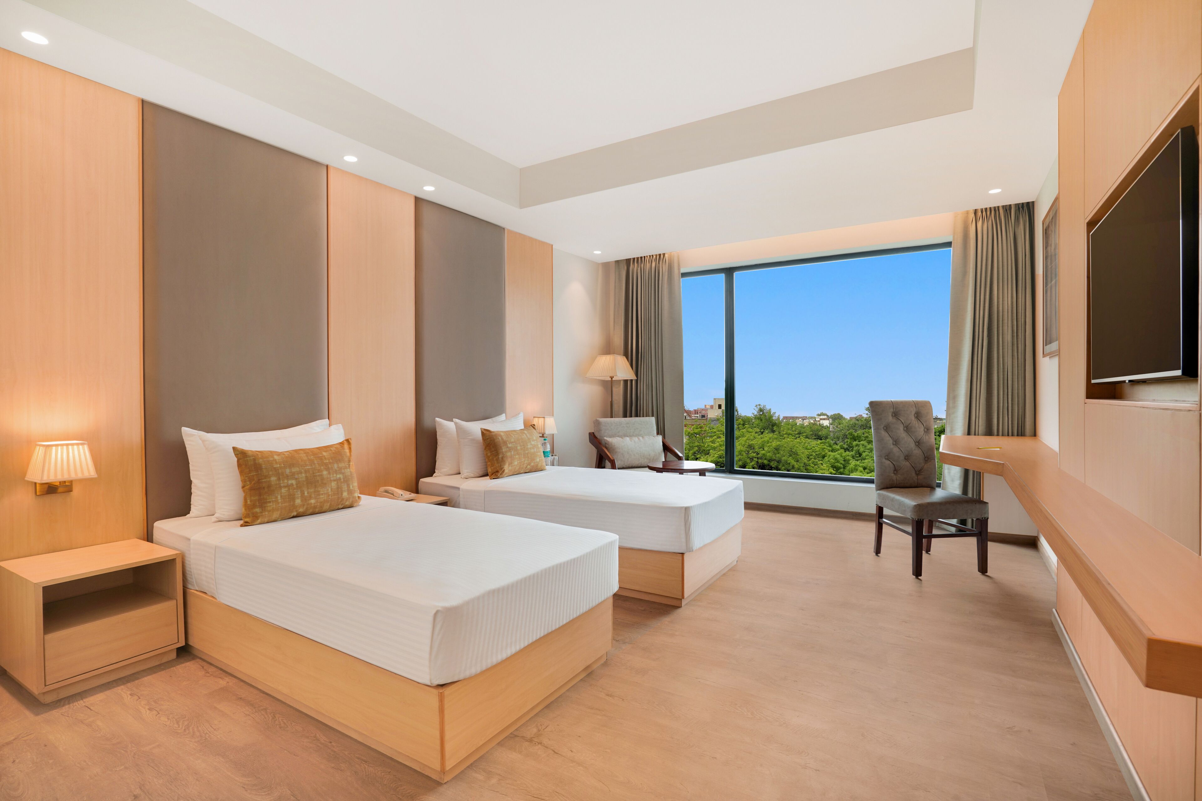 A hotel room with two beds, a TV, a chair, and a large window with a view.