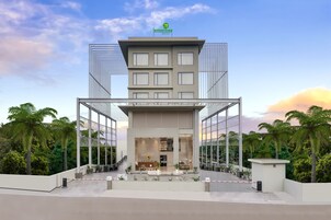 Hotel moderno com átrio central, fachada de vidro e um jardim no terraço.