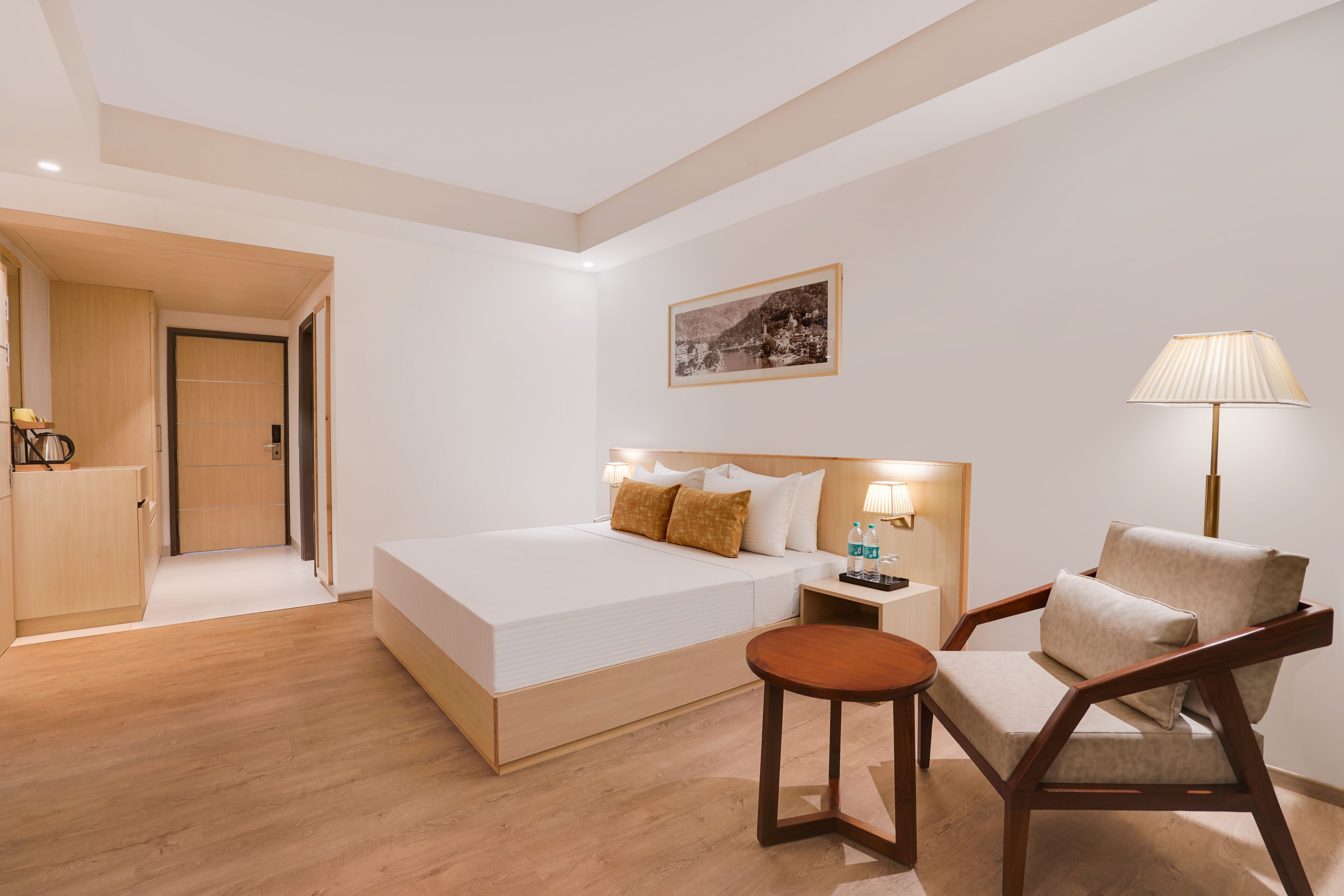 A modern hotel room with a large bed, bedside tables, a chair, and a painting on the wall.