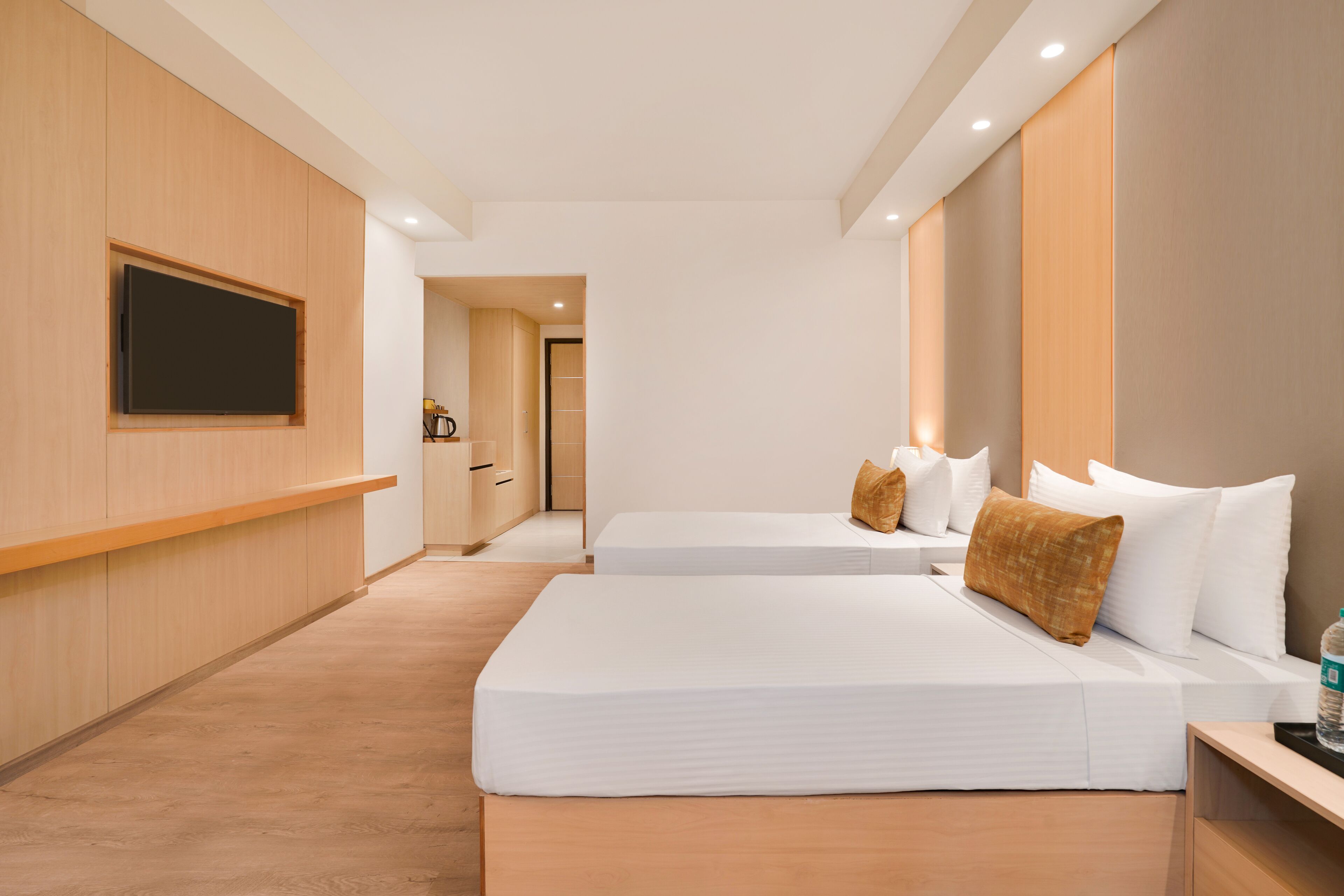 A hotel room with two beds, a flat-screen TV mounted on the wall, and a wooden floor.