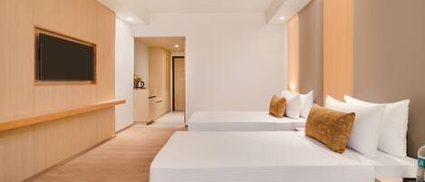 A hotel room with two beds, a flat-screen TV mounted on the wall, and a wooden floor.