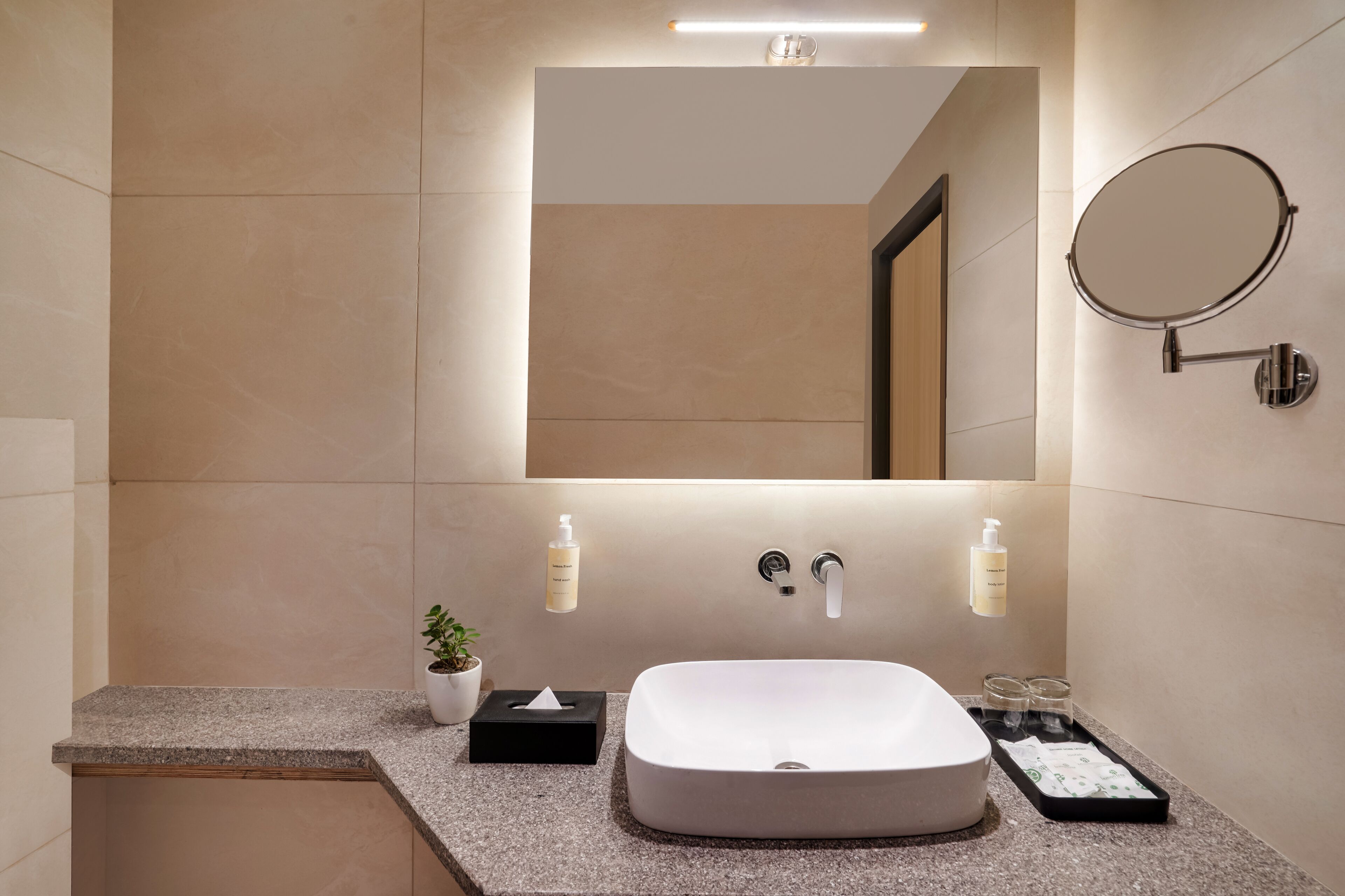 A modern bathroom with a large mirror, a white sink, and two wall-mounted soap dispensers.