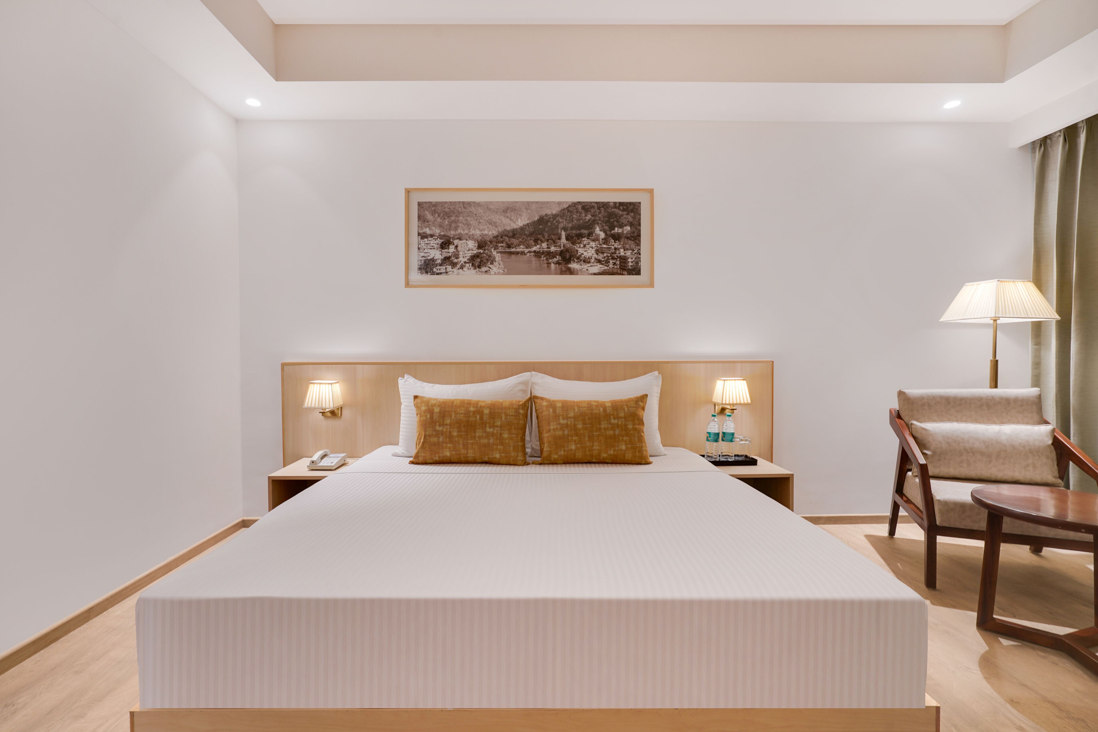 Une chambre d’hôtel avec un grand lit, une table de chevet avec une lampe, une chaise et un tableau encadré au mur.