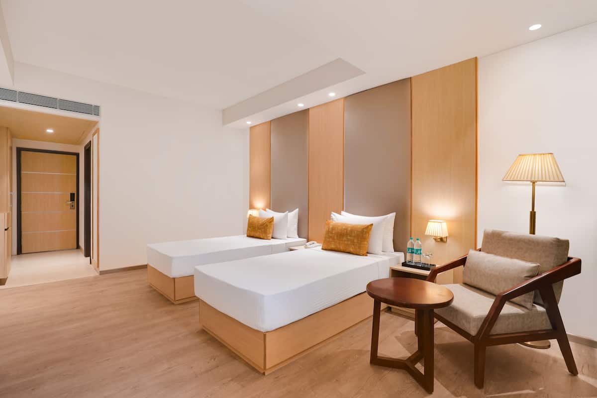 A modern hotel room with two single beds, a wooden nightstand, a lamp, and a wooden chair.