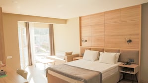 Habitació d'hotel moderna amb un llit gran, una taula de treball i una cadira. Hi ha una finestra amb cortines, una taula de nit amb una làmpada i un telèfon fixat a la paret.