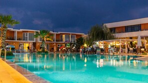 A swimming pool with lounge chairs and umbrellas, surrounded by buildings with multiple floors and balconies.