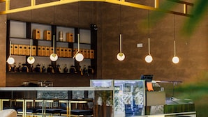Zona de bar moderna amb llums penjants, una barra amb una caixa registradora i cadires tapissades de verd.