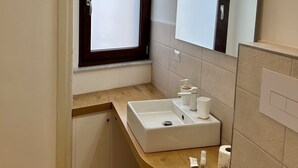 A small bathroom with a window, a sink, a mirror, and a toilet.
