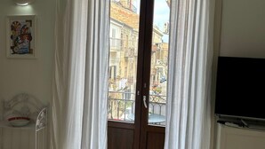 A hotel room with a balcony, a bed, a TV, and a painting on the wall.