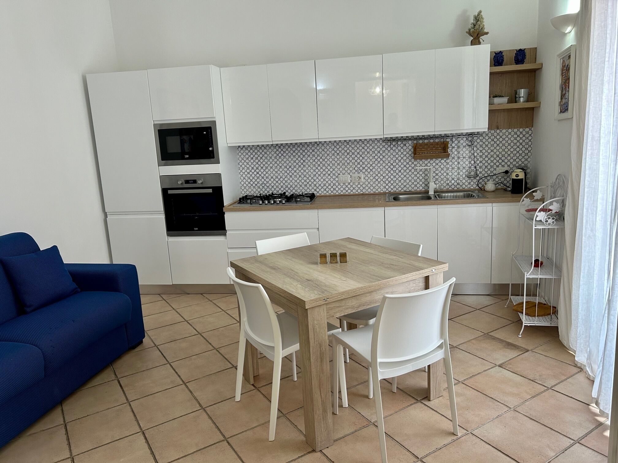A compact kitchen with white cabinets, a microwave, oven, and a gas stove. There is a dining table with chairs and a blue sofa in the living area.