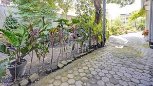 A covered outdoor area with a paved walkway, surrounded by various potted plants and trees. - OYO Life 92937 Kost Putri Sarkara Syariah (Rogojampi)