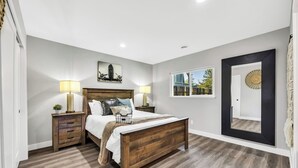 A bedroom with a wooden bed, two bedside tables with lamps, a large window, and a door with a decorative mirror. - Modern&Comfy|EV Charger|Kids&Pets| quick 80 access (Auburn)