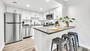 A modern kitchen with white cabinets, stainless steel appliances, and a central island with stools. - Modern&Comfy|EV Charger|Kids&Pets| quick 80 access (Auburn)