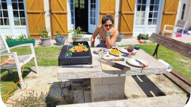 Una persona sentada en una mesa al aire libre con una parrilla, comida y bebidas.