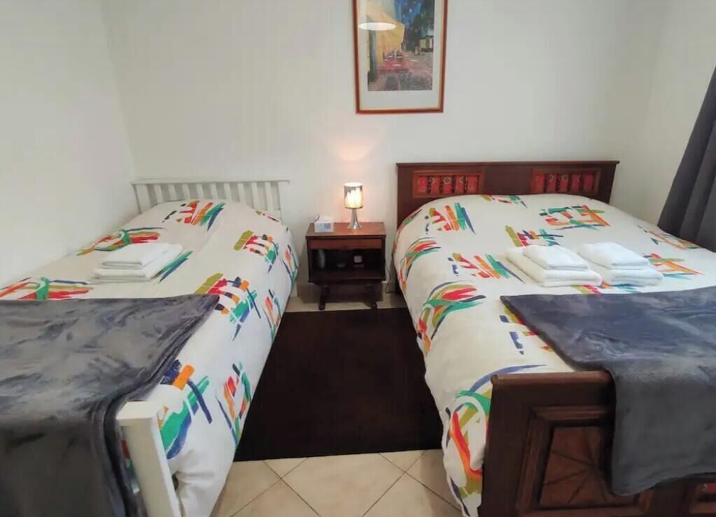 Een hotelkamer met twee eenpersoonsbedden, een nachtkastje, een lamp en een lijst met een foto aan de muur.