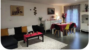 Una sala de estar con sofá, mesa de centro, mesa de comedor con sillas y un aparador.