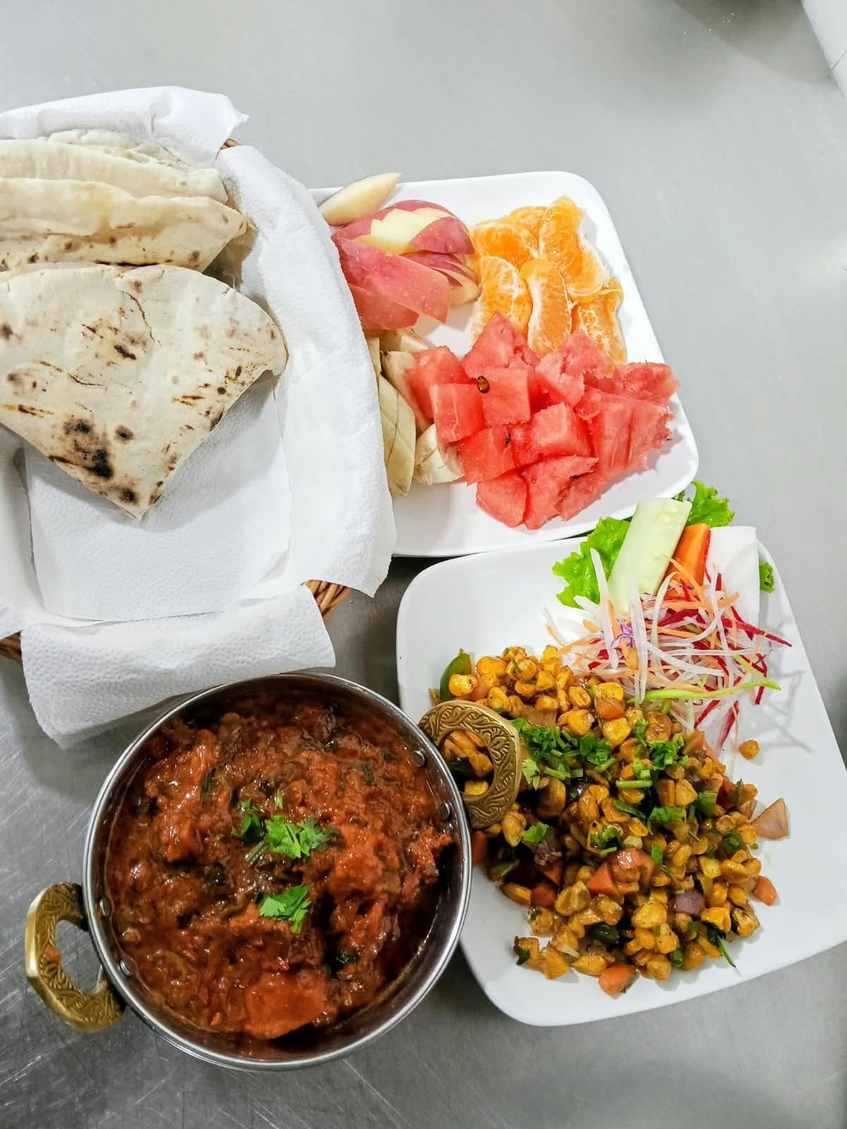 A meal with naan bread, fruit, salad, and a bowl of curry.