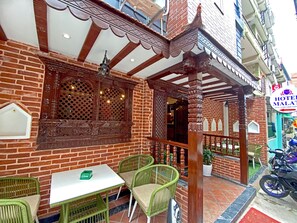 Un bâtiment traditionnel avec une façade en briques, des sculptures en bois et un balcon agrémenté de chaises et d’une table en osier vert.