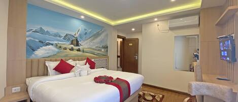 A modern hotel room with a large bed, a mounted television, and a mural of a mountainous landscape.