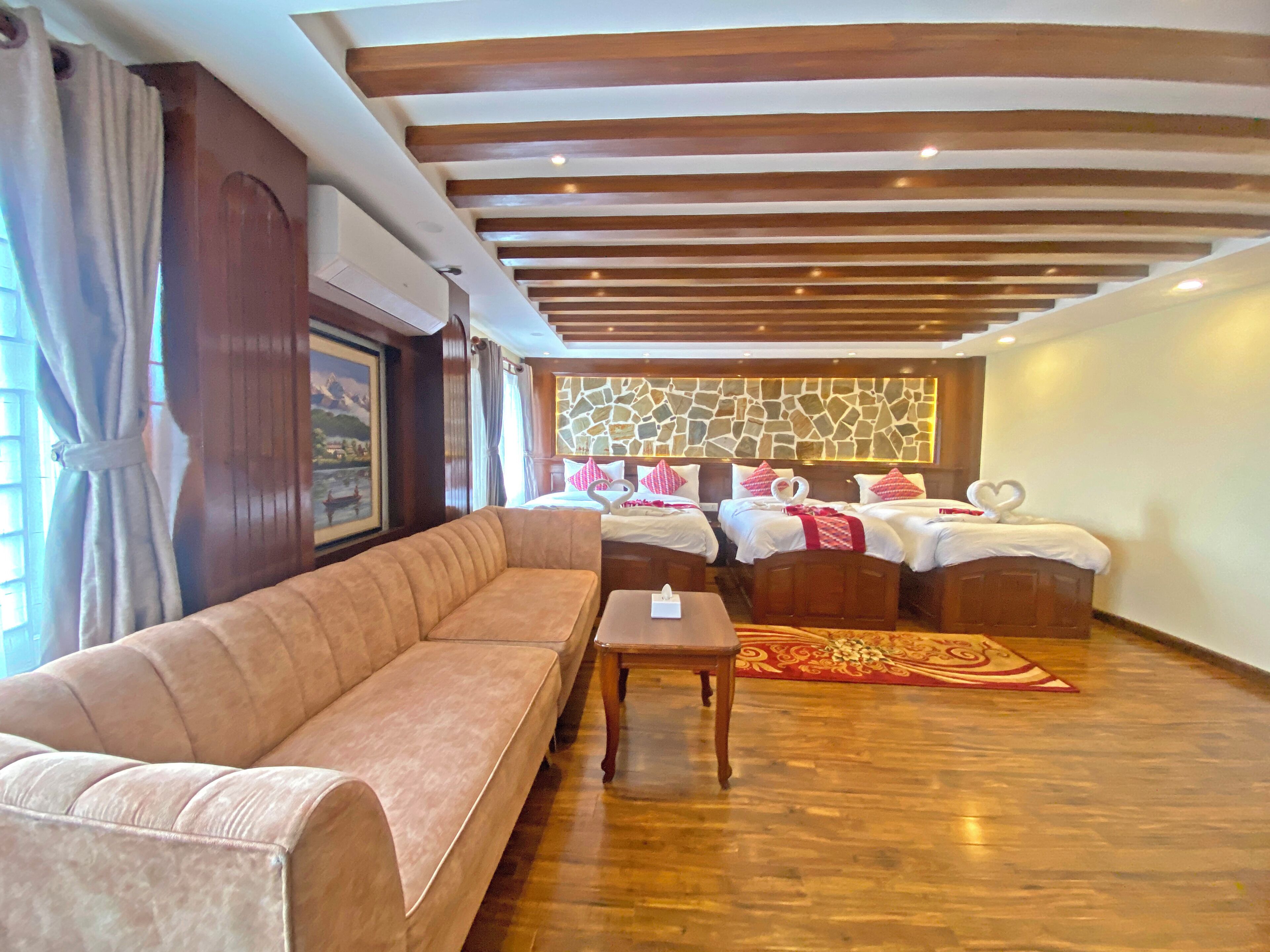 A hotel room with a sofa, two beds, a stone wall, and a wooden ceiling.