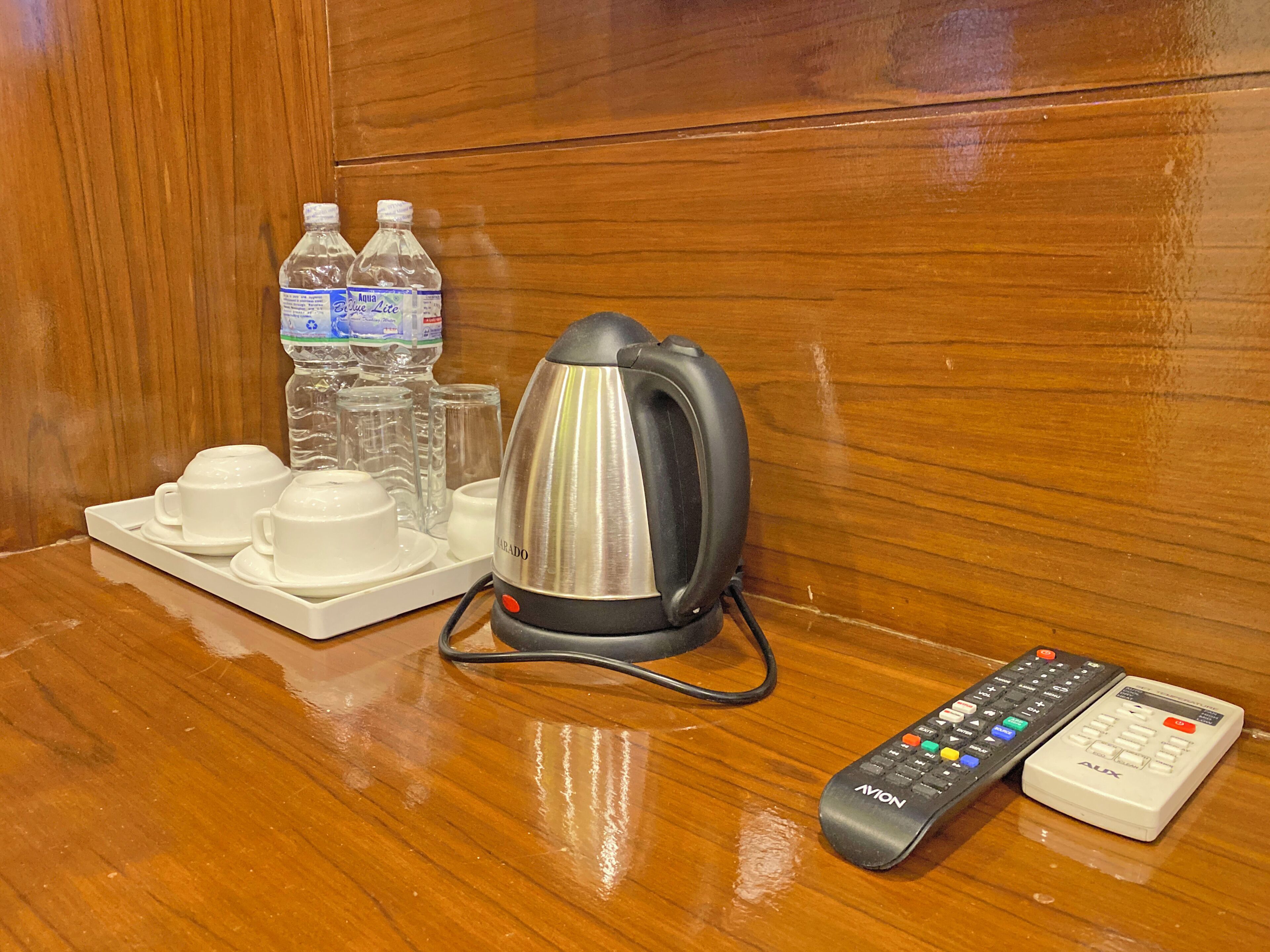 Habitación de hotel con tetera, tazas, control remoto y agua embotellada sobre una bandeja.