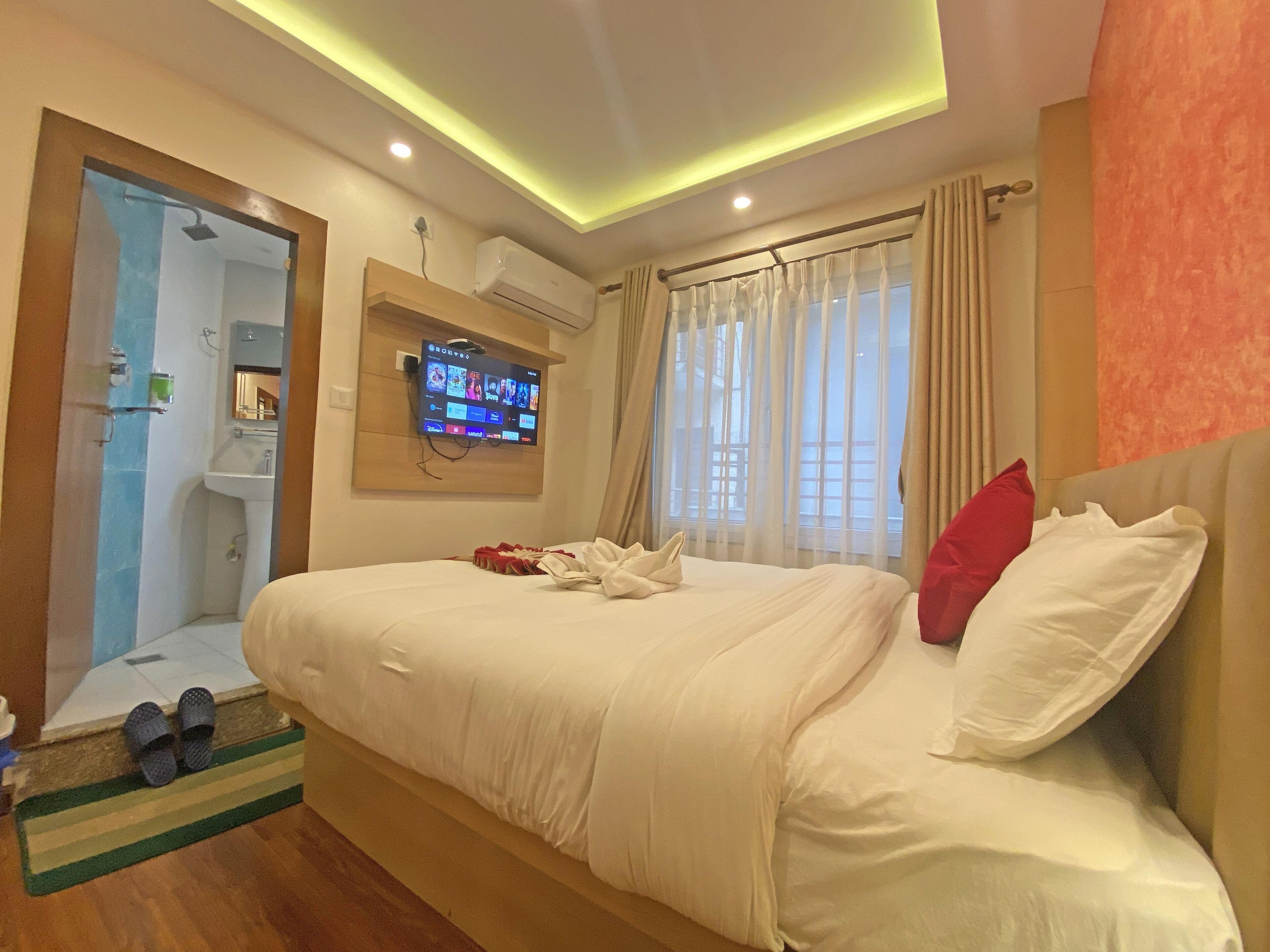 Ein Hotelzimmer mit Bett, Wand-Fernseher, Klimaanlage, Badezimmer mit Dusche und einem Vorhangfenster.