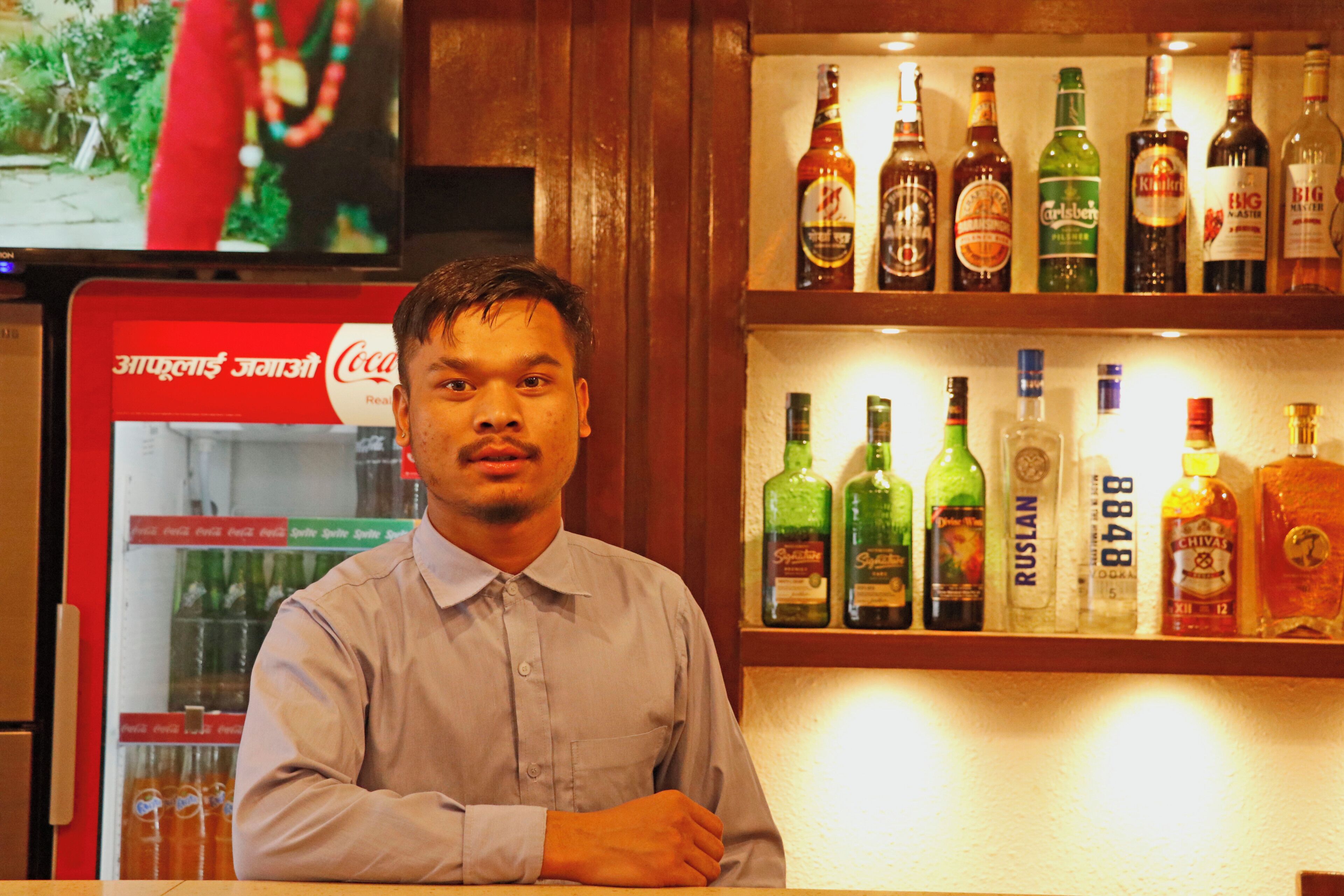 A man standing in front of a bar with shelves of liquor bottles.