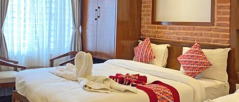 Habitación de hotel con techo de madera, pared de ladrillo, una cama grande con ropa blanca, dos mesitas de noche y una ventana con cortinas.
