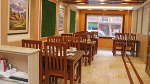 A dining area with wooden tables and chairs, framed pictures on the walls, and a window with a view of the street. - Hotel Malati (Kathmandu)