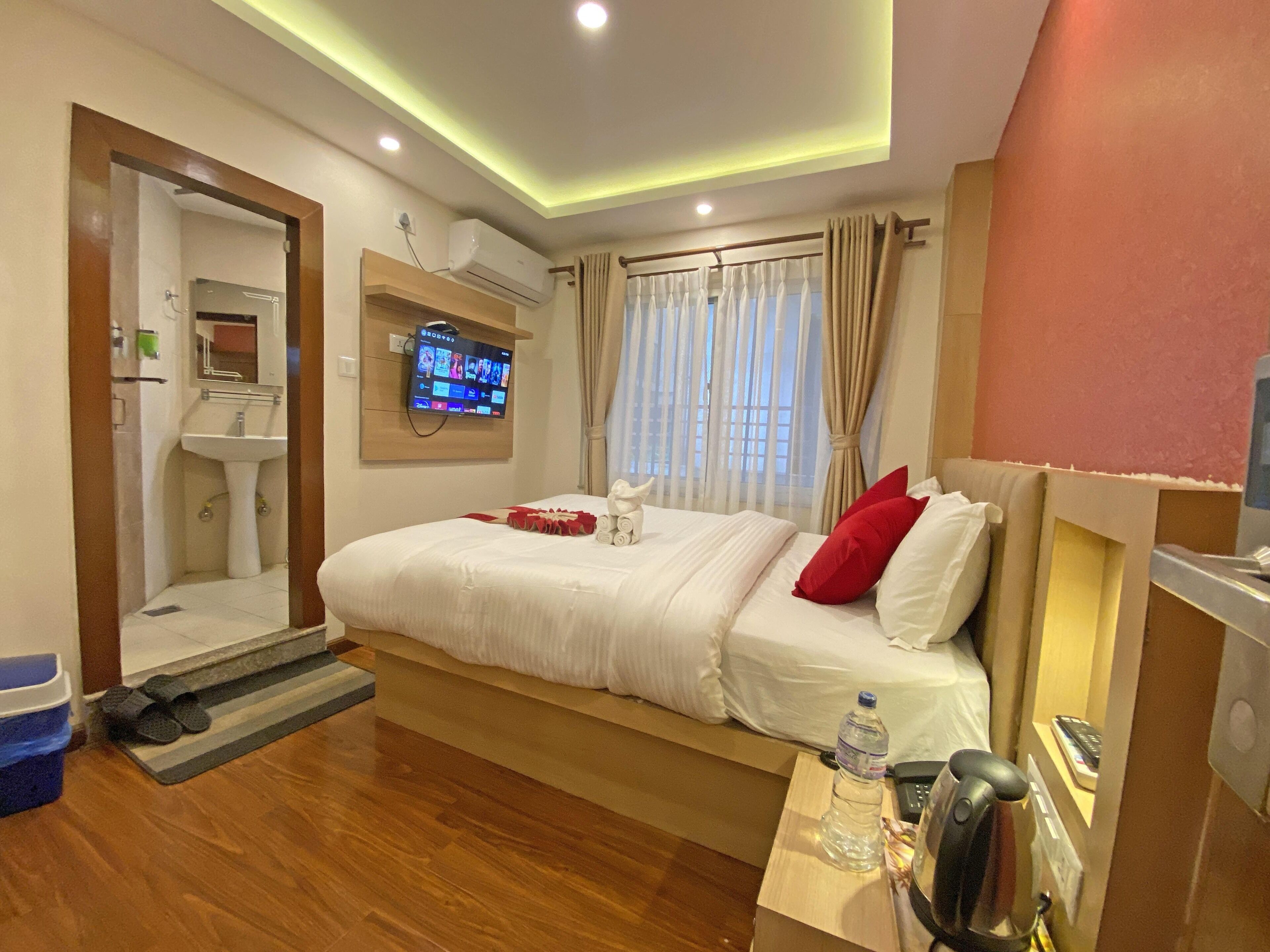 A hotel room with a bed, a TV mounted on the wall, a sink, and a window with curtains.