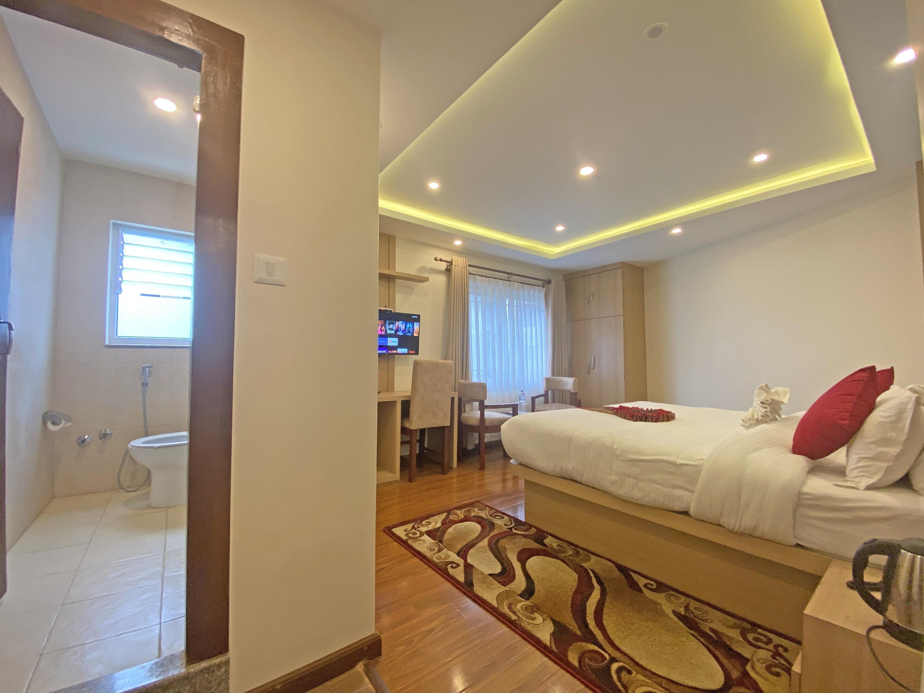Habitación de hotel con una cama grande, un escritorio con silla, televisión y un baño visible a través de una puerta abierta.