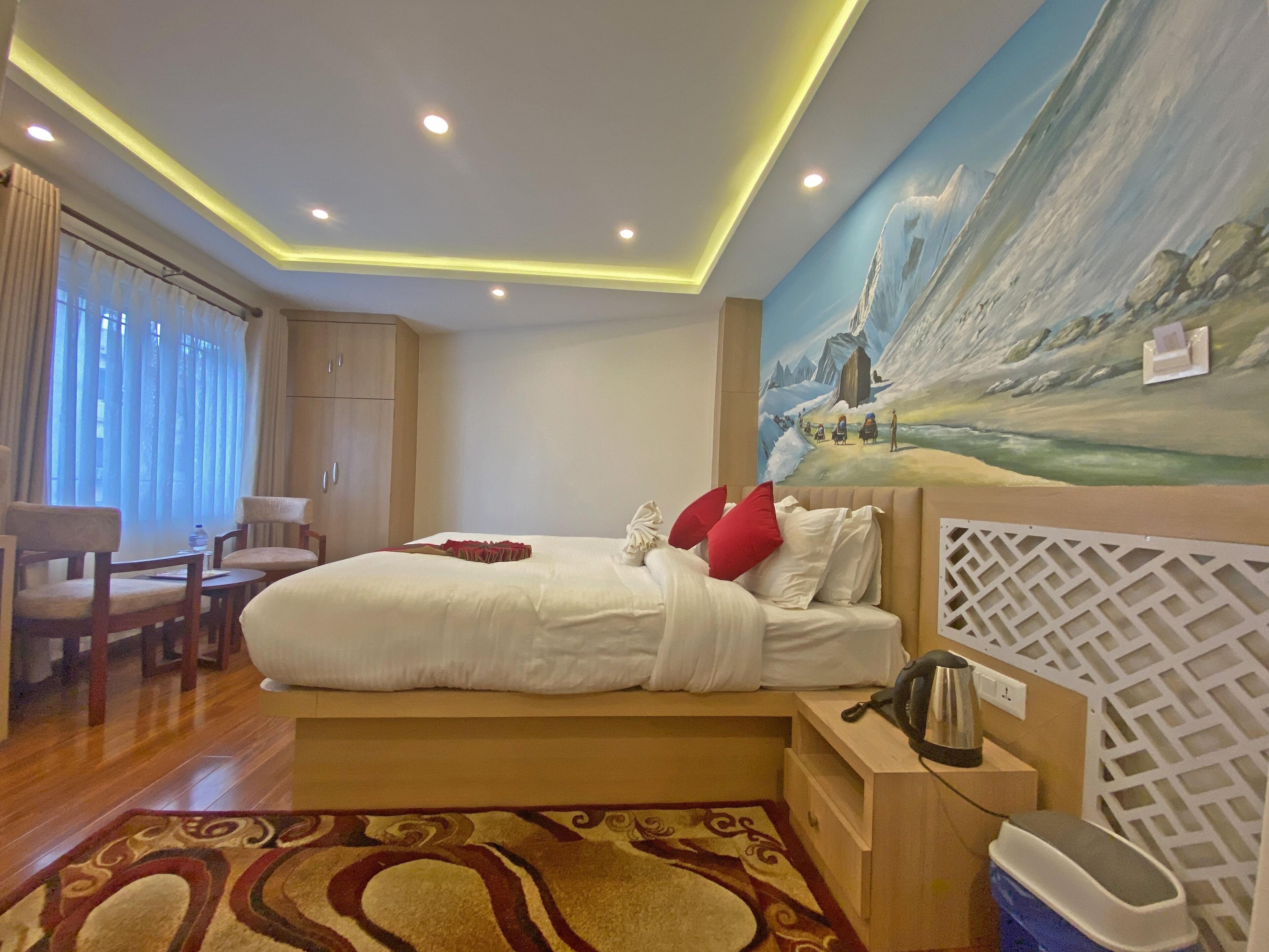 A hotel room with a bed, a desk, a chair, a painting on the wall, and a window with curtains.