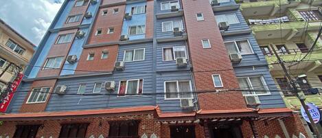 Un edificio a più piani con facciate in mattoni e dipinte, numerosi balconi e un ingresso a livello strada con portico.