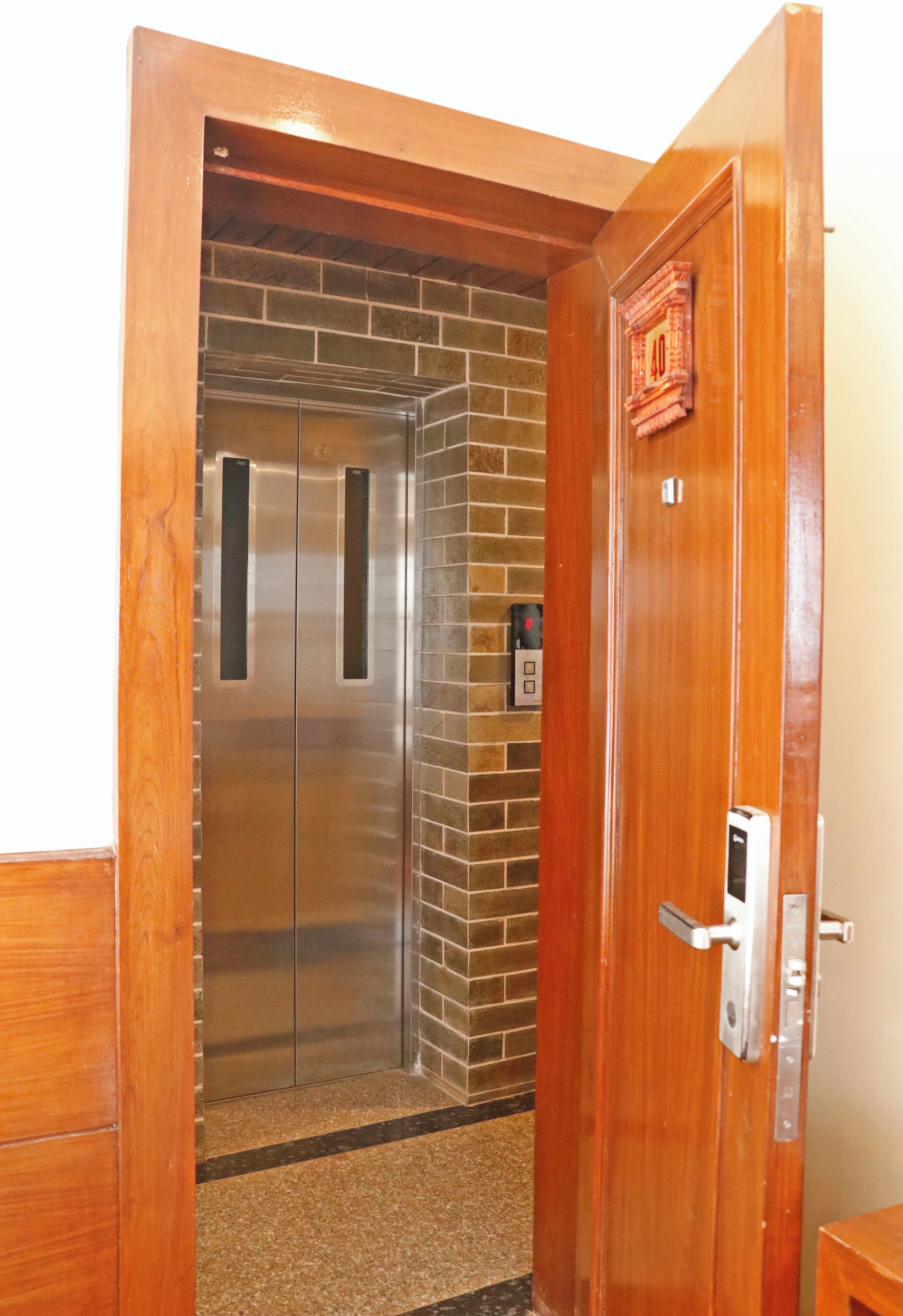 An elevator with a metallic finish, a wooden door frame, and a small red decoration on the wall.