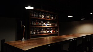 Una zona de bar con una larga barra de madera y estanterías llenas de botellas.