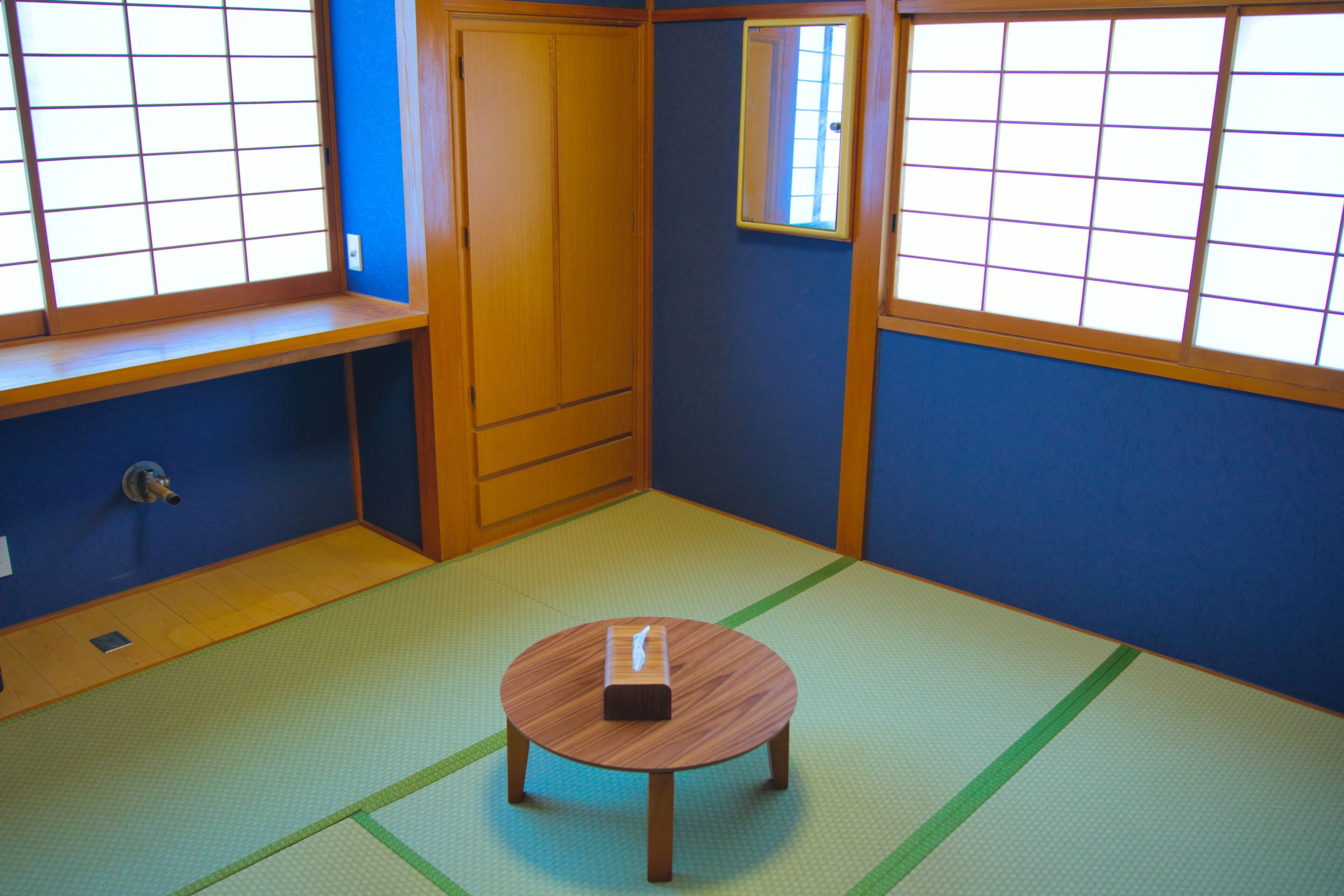 A tatami mat room with a wooden table, a wardrobe, and a window with a grid pattern.