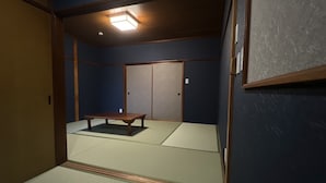 Una habitación japonesa tradicional con suelo de tatami, una mesa de madera baja, puertas correderas y una lámpara en el techo.