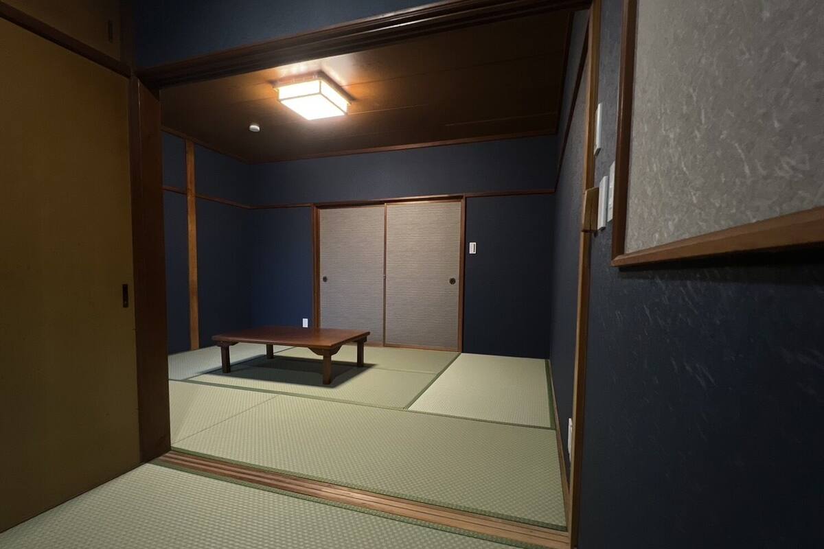 A traditional Japanese room with tatami flooring, a low wooden table, sliding doors, and a ceiling light fixture.