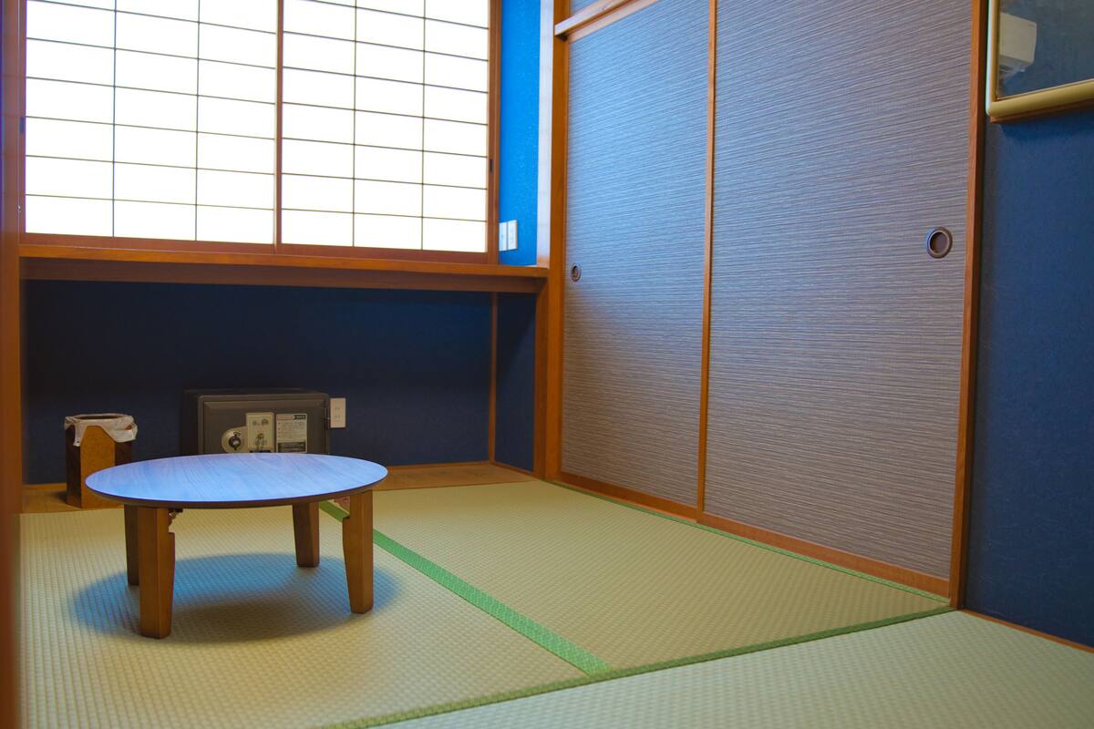 A tatami mat room with a low table, a sliding door, and a window with grid patterns.