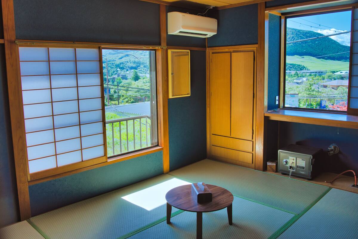 A traditional Japanese room with tatami flooring, a shoji screen, a sliding door, and a view of a mountainous landscape.