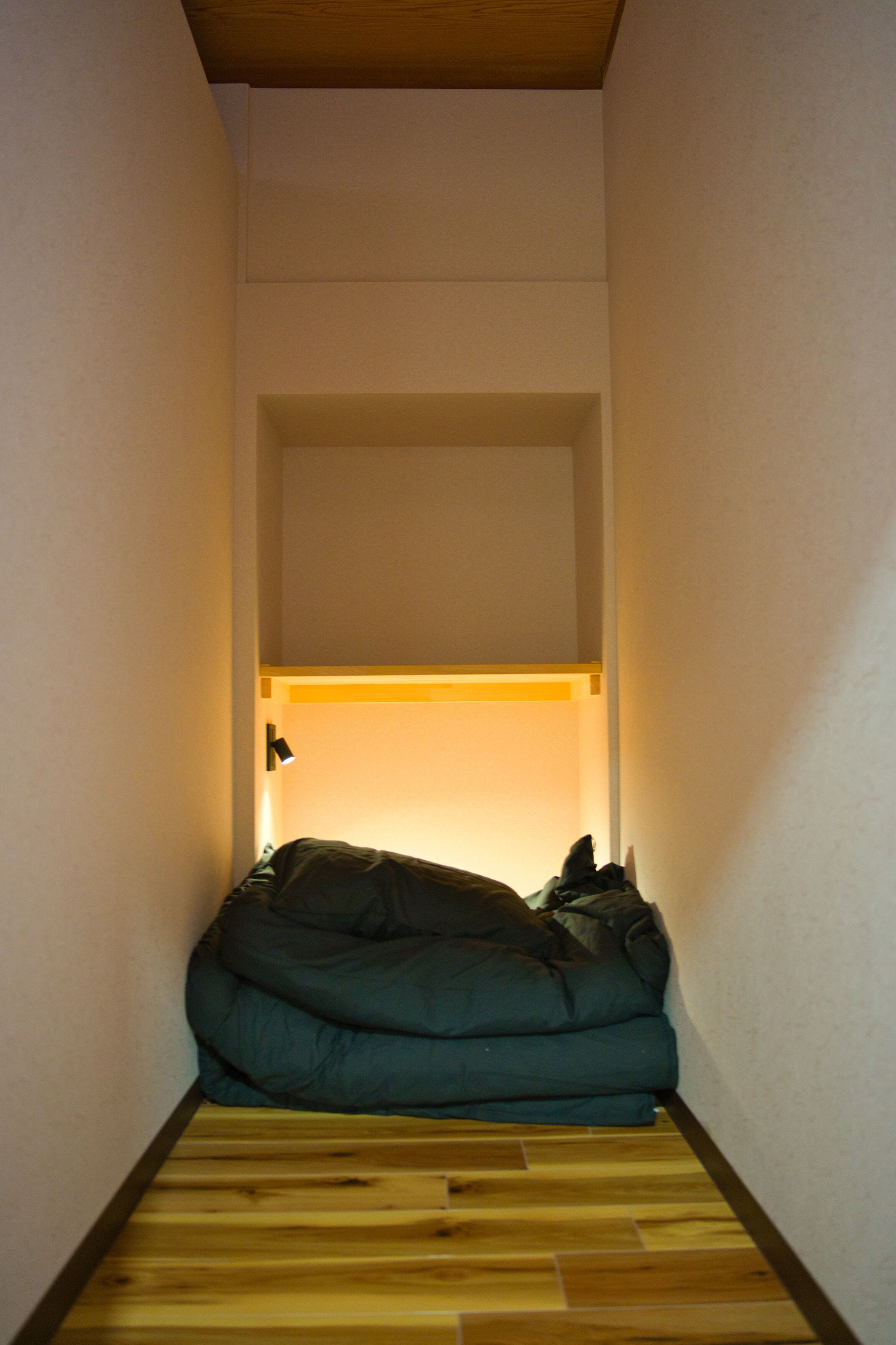 A narrow room with a wooden floor and a bed at the end.