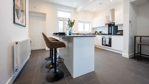 A modern kitchen with a central island, bar stools, a built-in oven, and a large window providing natural light. - Durham View by Tŷ SA (Newport)
