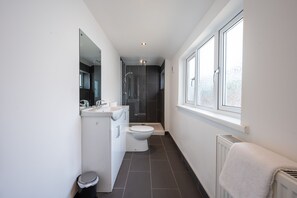 A narrow bathroom with a toilet, sink, and shower area. - Durham View by Tŷ SA (Newport)