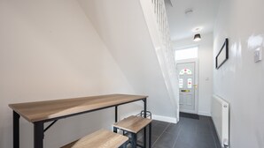 A narrow hallway with a wooden table and two stools, a white door with a decorative glass panel, and a white radiator on the wall. - Durham View by Tŷ SA (Newport)