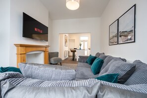 A modern living room with a grey sofa, teal cushions, a flat-screen TV, and a fireplace. - Durham View by Tŷ SA (Newport)