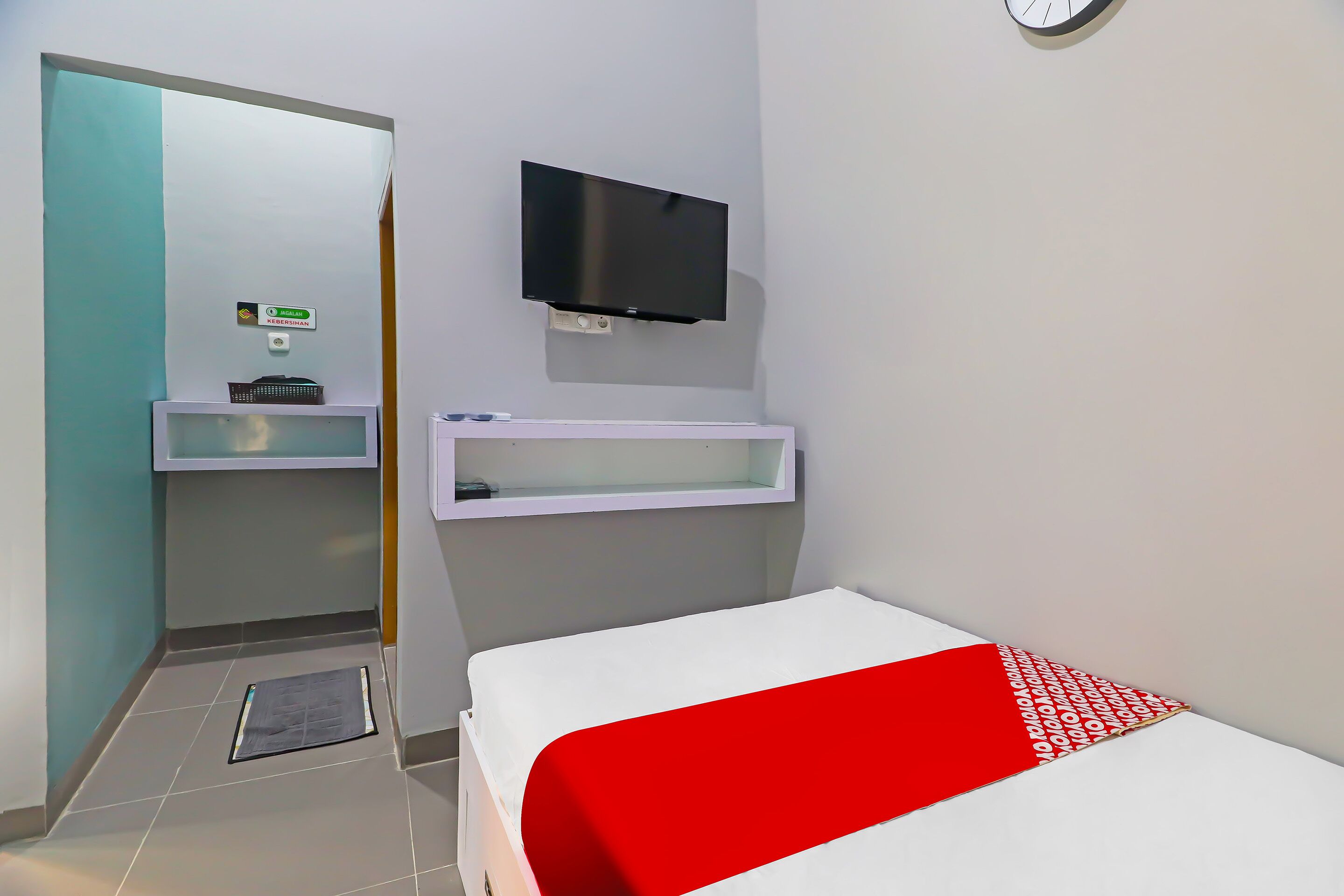 Ein Hotelzimmer mit einem Bett, einem an der Wand montierten Fernseher, einem kleinen Schreibtisch mit Stuhl und einem Spiegel.