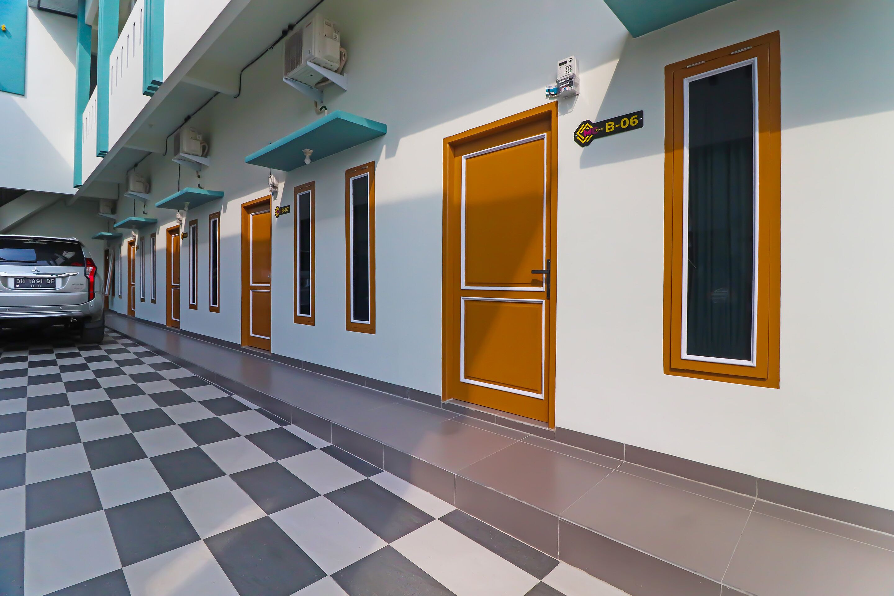 A hotel corridor with checkered flooring, doors with brown frames, and a parked car.